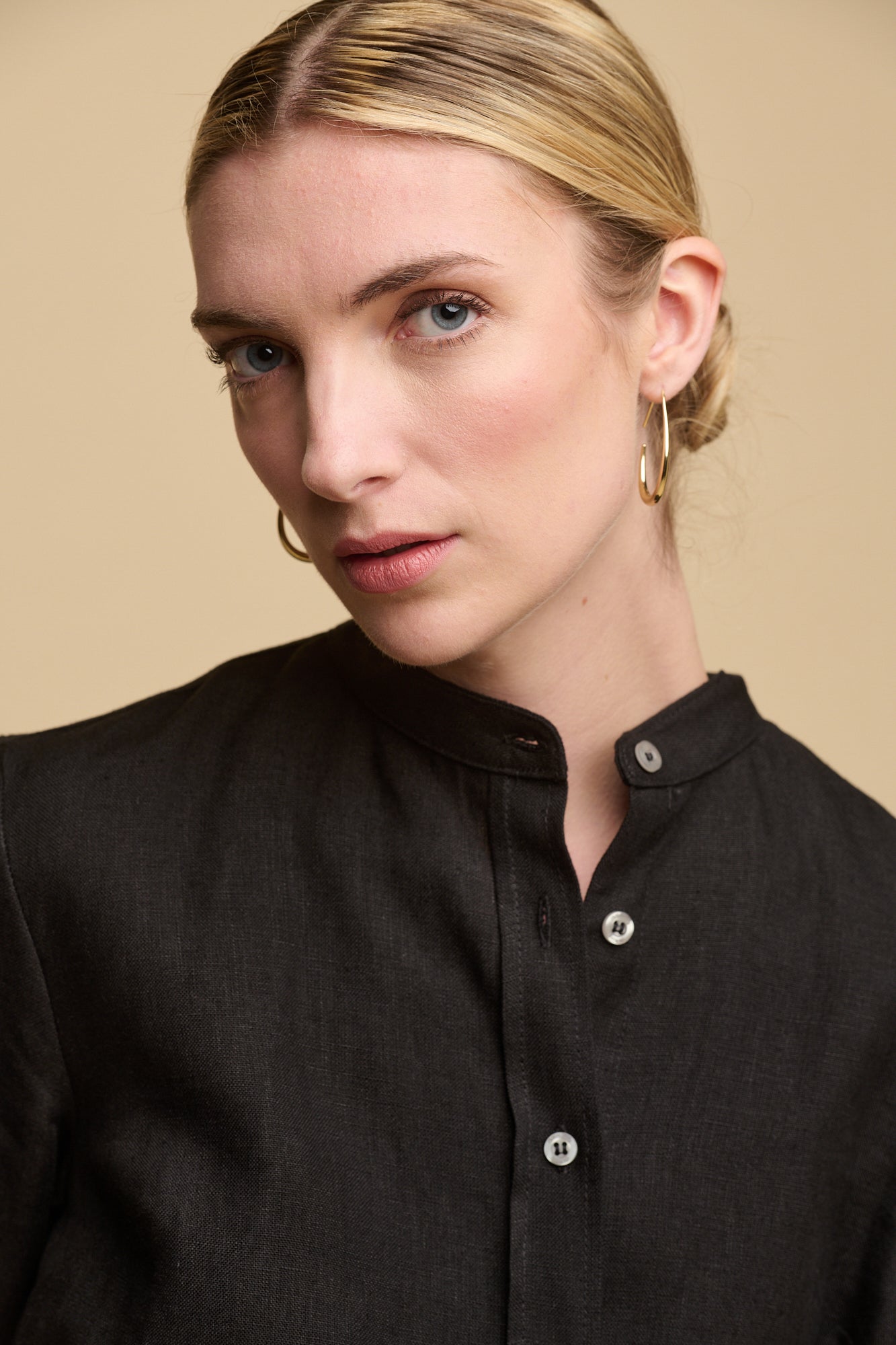 Portrait of blonde female with hair tied back in bun wearing collarless shirt dress in black linen