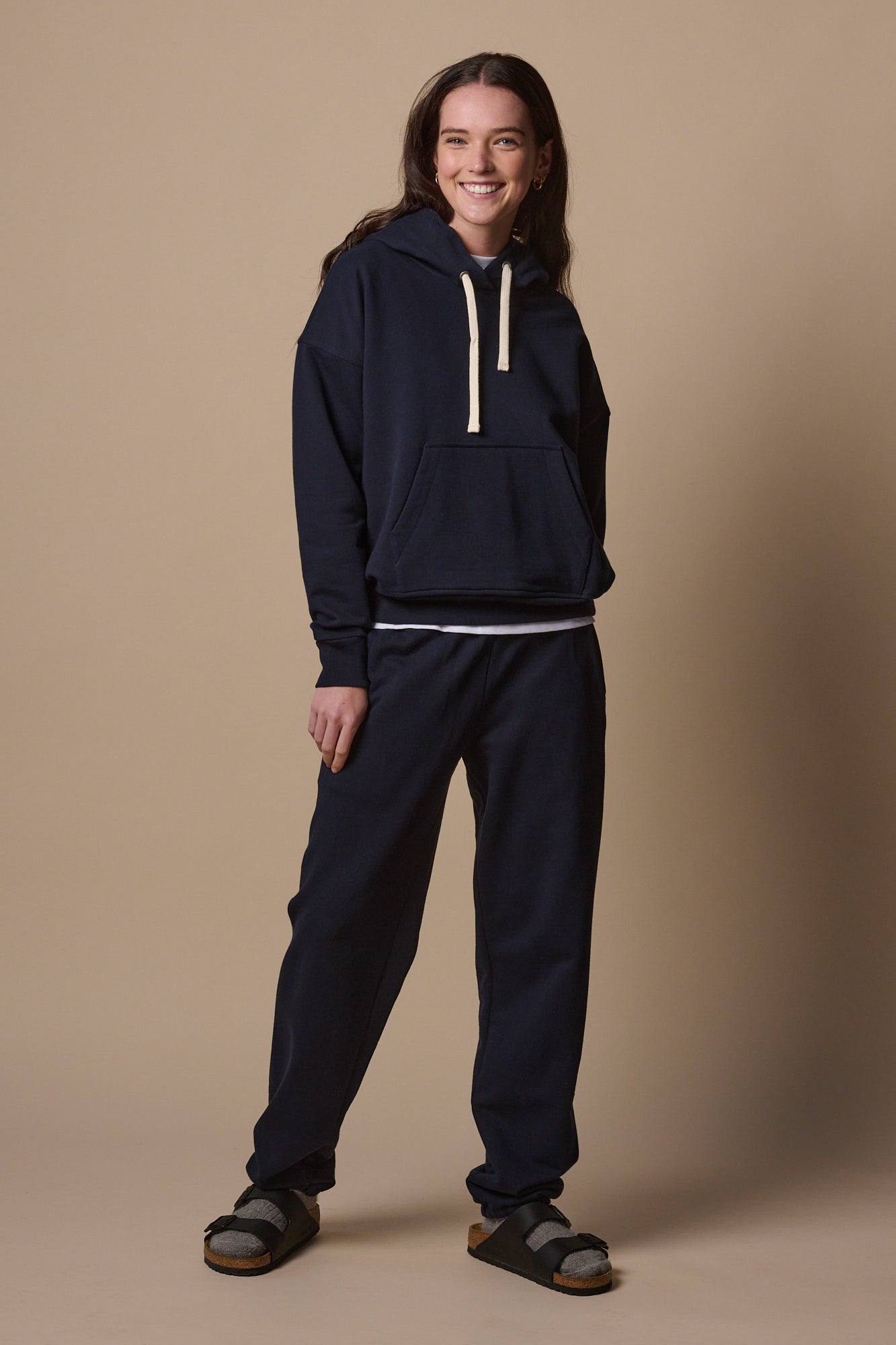 Full body image of female wearing hooded sweatshirt in navy with matching navy sweatpants