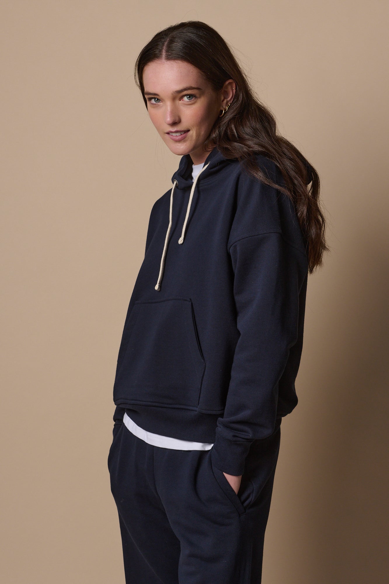 Thigh up image of female wearing hooded sweatshirt in navy with ecru drawstring through the hood, one central front pocket