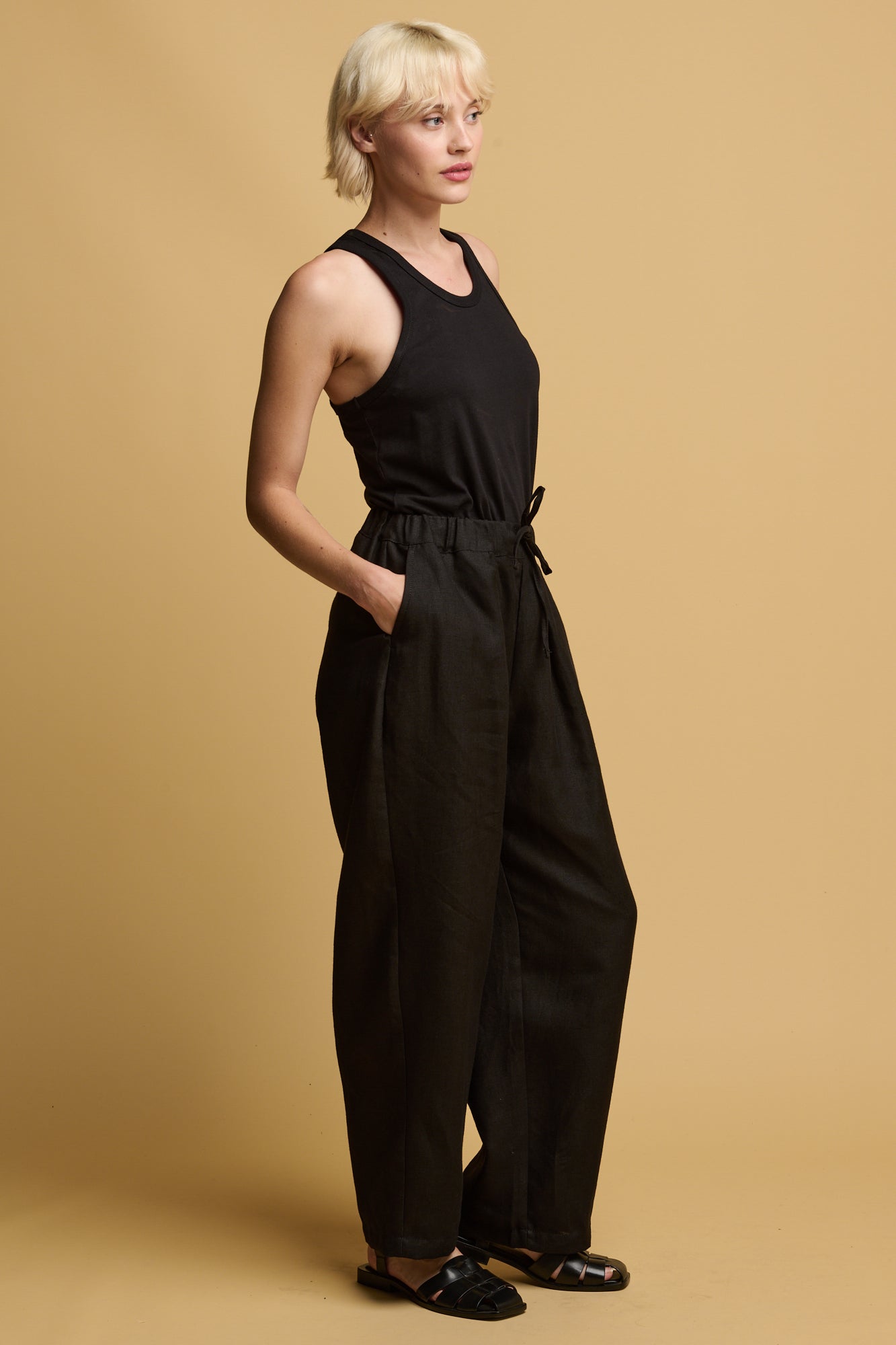 The side of blonde female wearing lorna elasticated waist linen trousers in black with her hand in the front pocket 