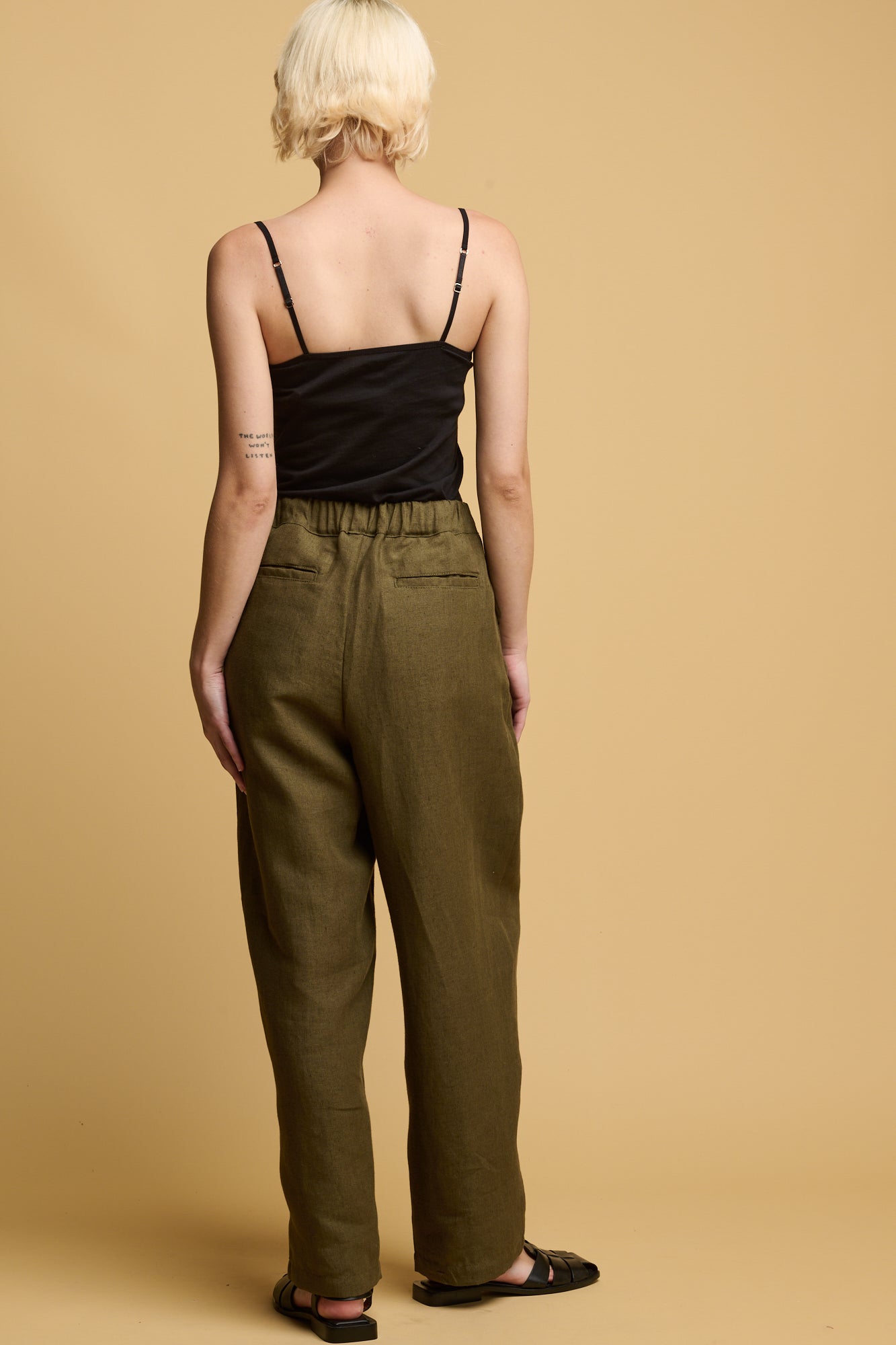 The back of a white female with short blonde hair wearing Community Clothing Lorna elasticated waist linen trousers in olive with two back jet pockets 