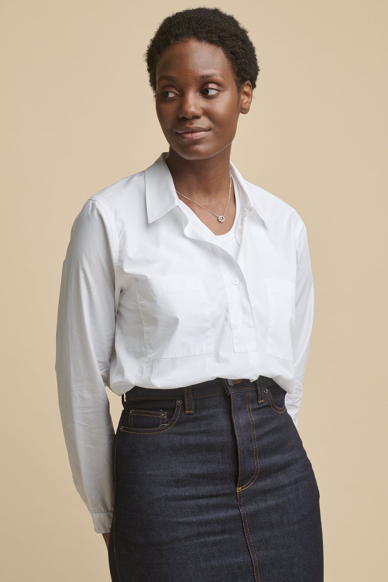 Thigh up image of the front of black female wearing Olivia half placket lightweight cotton shirt in white, worn over racer back vest in white paired with Maxi skirt in indigo