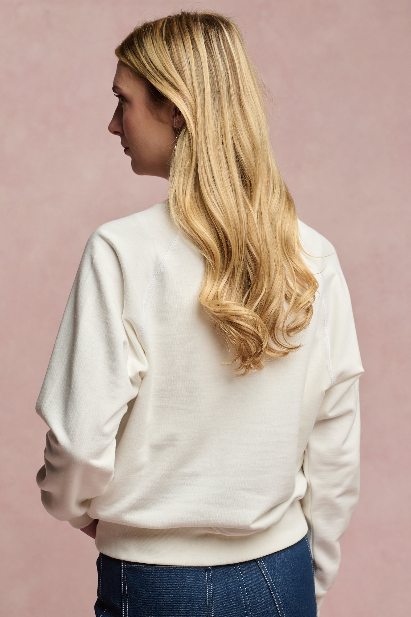 Thigh up image of the back of female with long blonde hair wearing raglan sweatshirt in bone