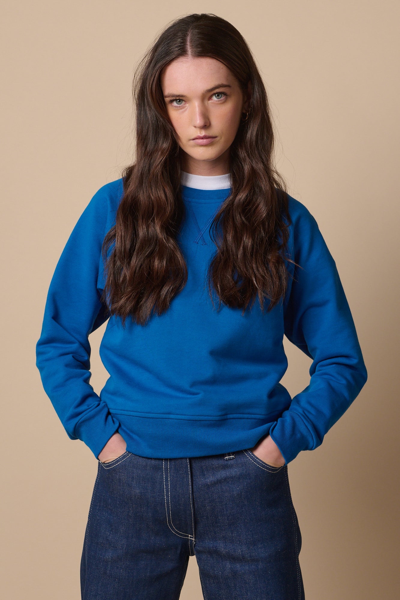 Female with long brown hair wearing raglan sweatshirt in cobalt with hands in jean pockets