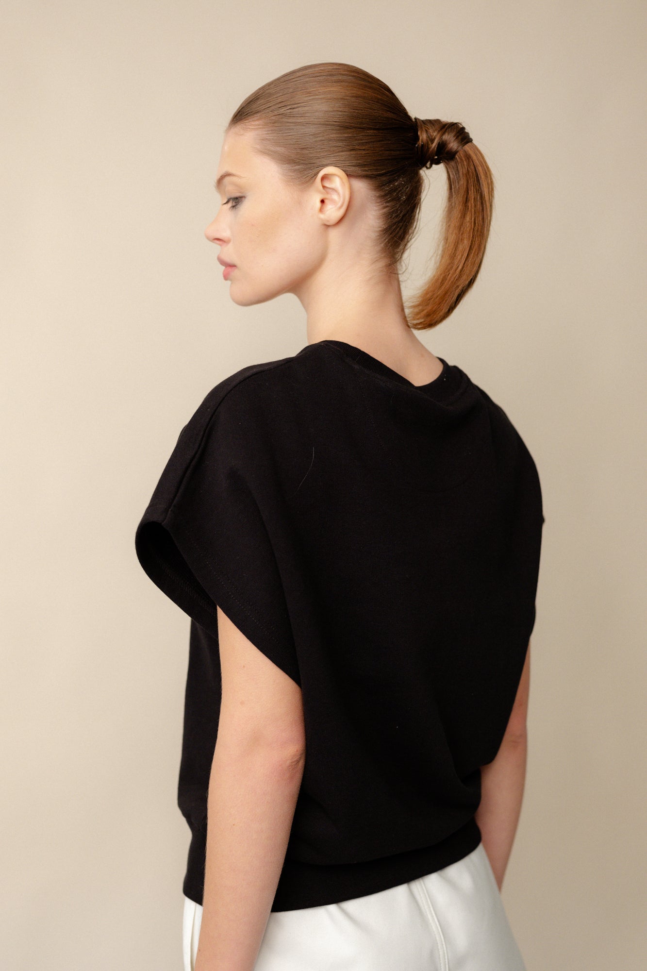 Hip up image from behind of white, brunette female wearing sleeveless sweatshirt plastic free in black.