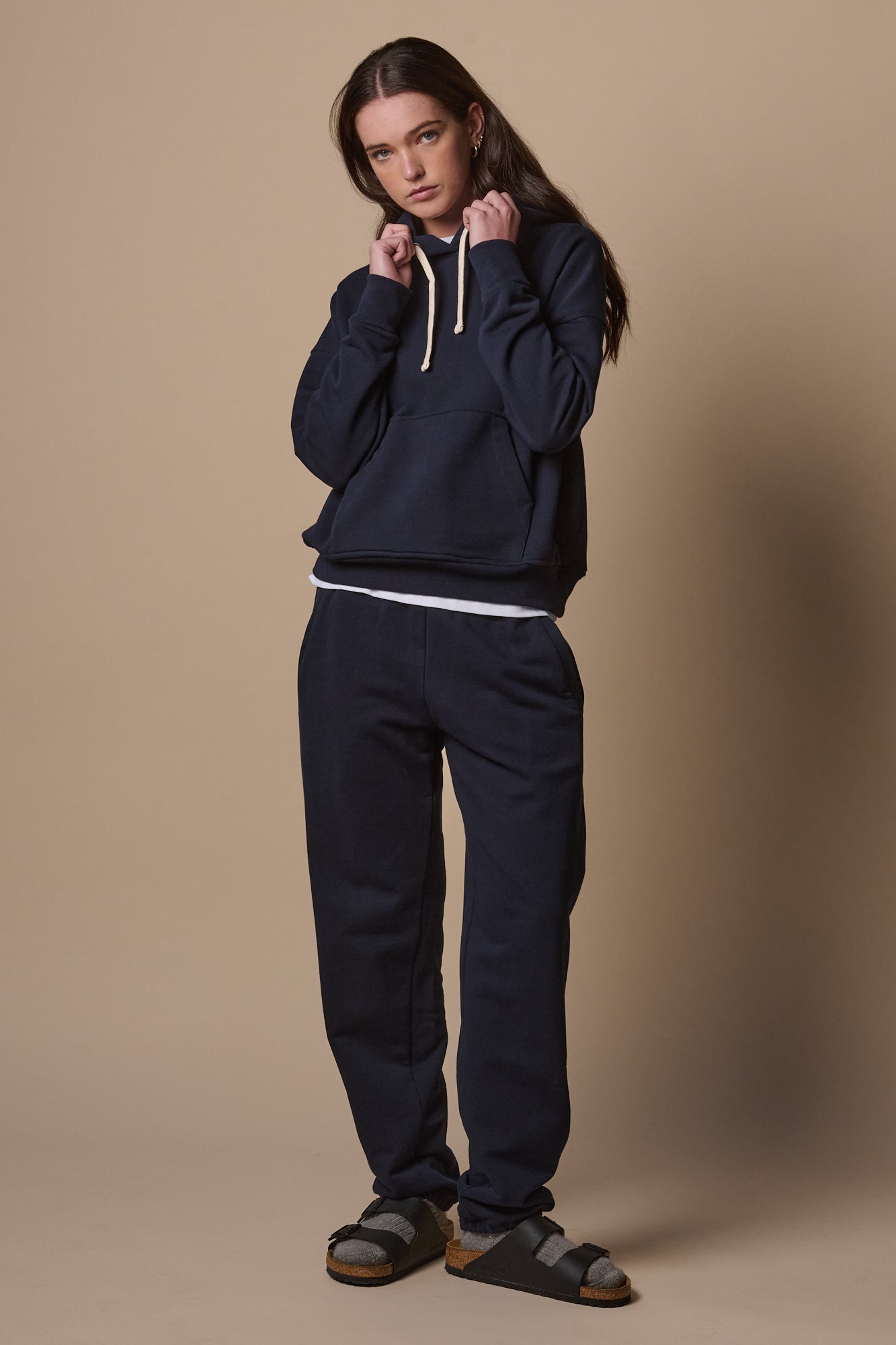 Full body image of female wearing sweatpants in navy paired with matching hooded sweatshirt 