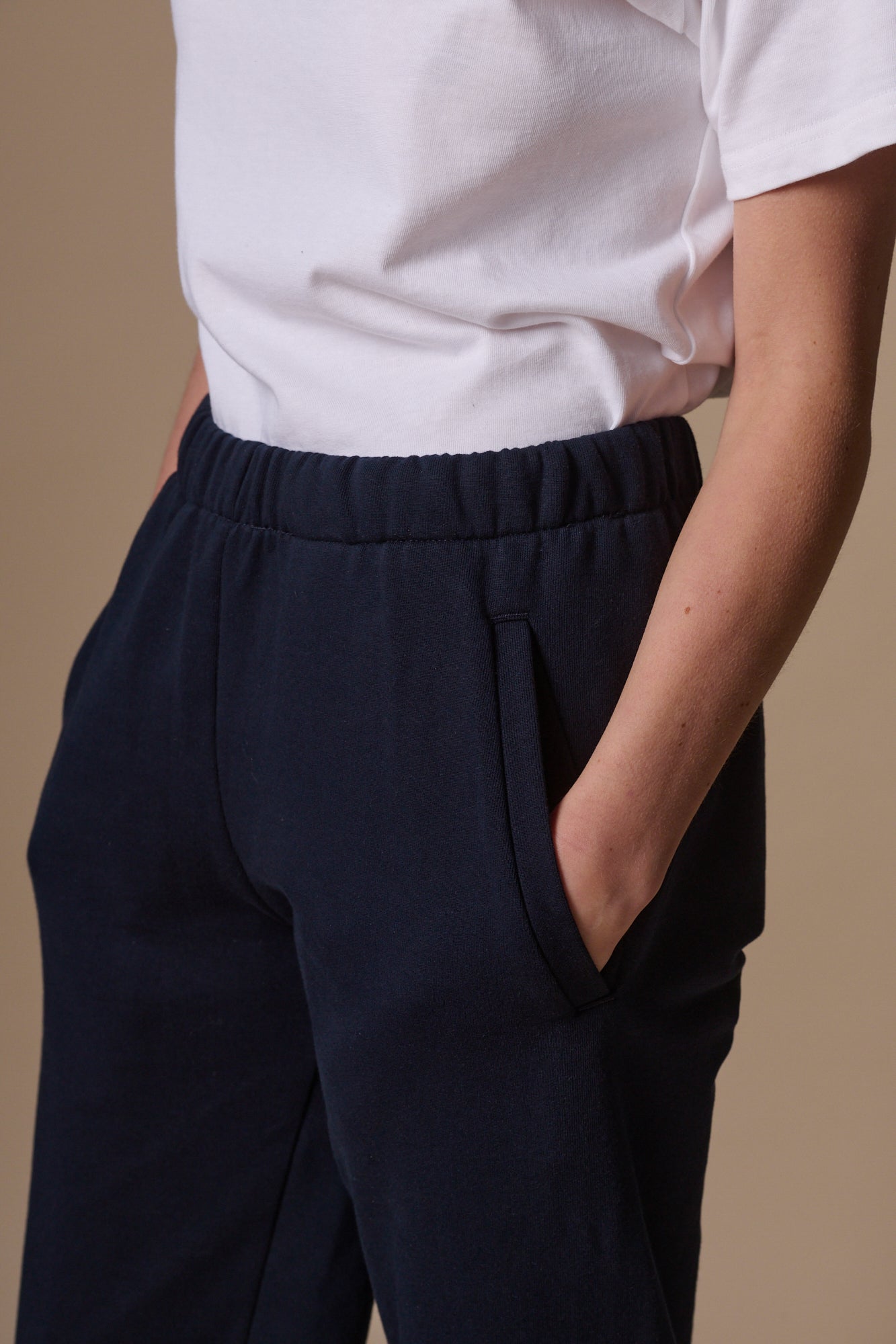 female with hands in two front pockets of sweatpants showing elasticated waistband, white t shirt tucked in  